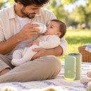 Pai dando mamadeira ao bebê no parque com o Tepio ao lado
